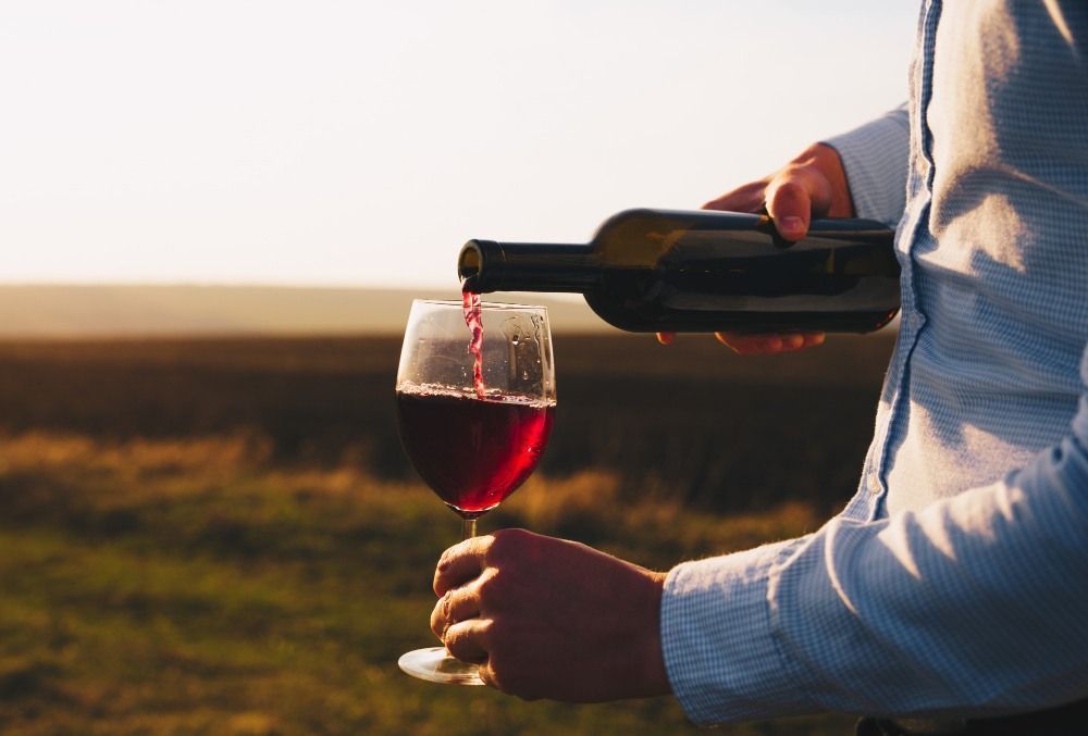 Personne qui a versé du vin rouge dans un verre au coucher du soleil