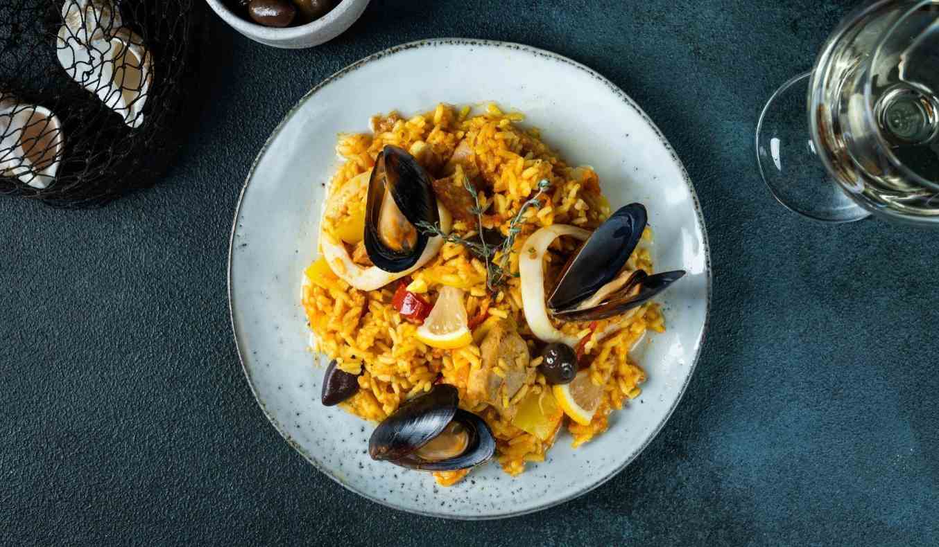 Assiette de paella avec des moules et des crevettes accompagné d'un verre de vin