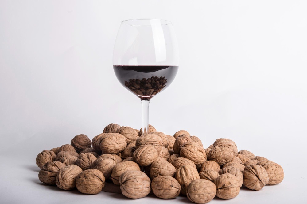 Verre de vin rouge posé sur un tas de noix entières, sur fond blanc