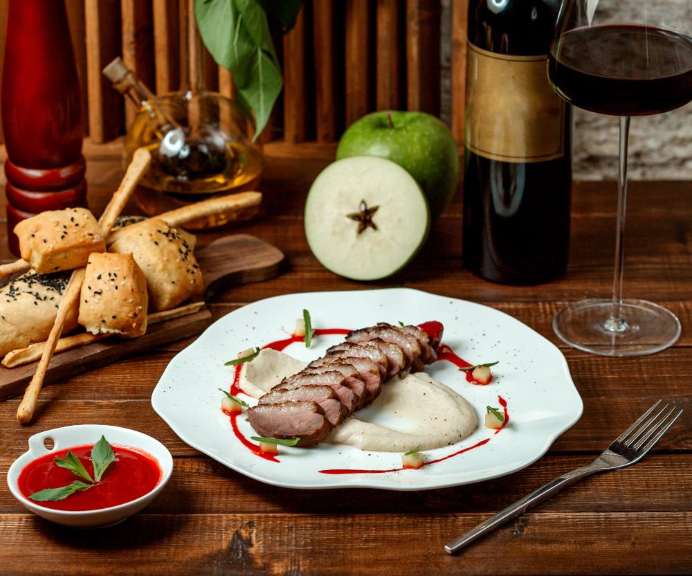 Magret de canard sauce fruits rouges, purée crémeuse et vin rouge : accord mets et vins gastronomique sur table en bois.