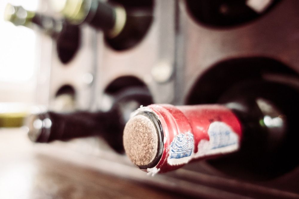 Bouteille de vin stockée horizontalement dans une cave à vin en bois, gros plan sur le bouchon et la capsule rouge.